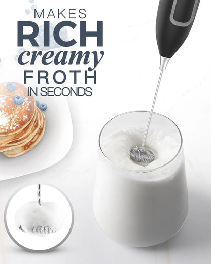 Electric frother being used to create froth in a glass of milk with pancakes in the background.